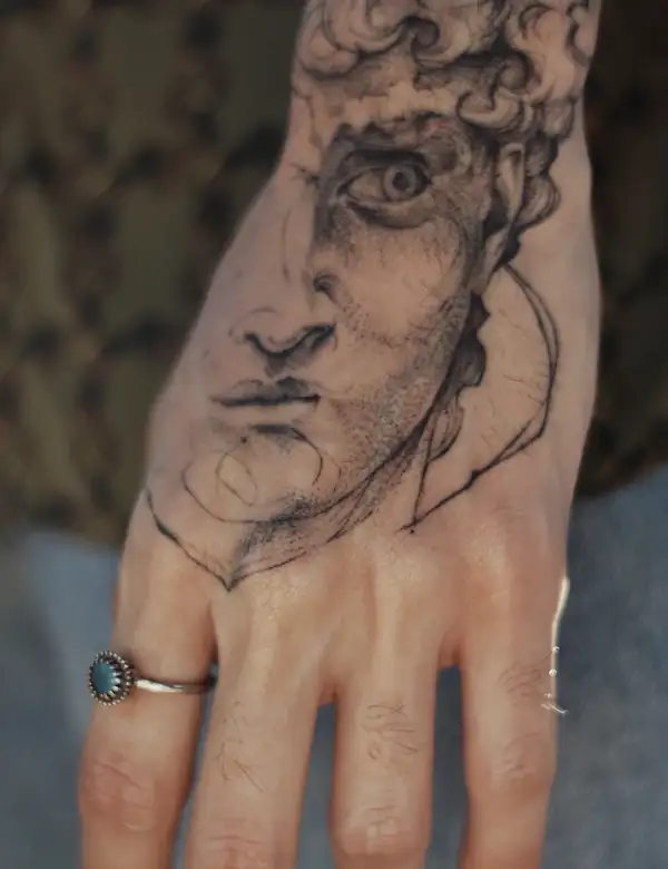 A fine-line sketch of a classical face on the back of a hand