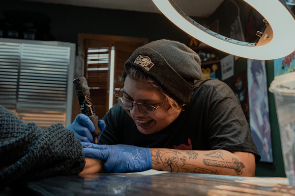 An artist smiling as he works on a client's arm