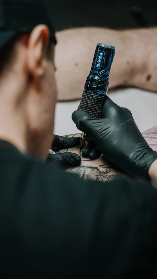 An artist tattooing with a black machine