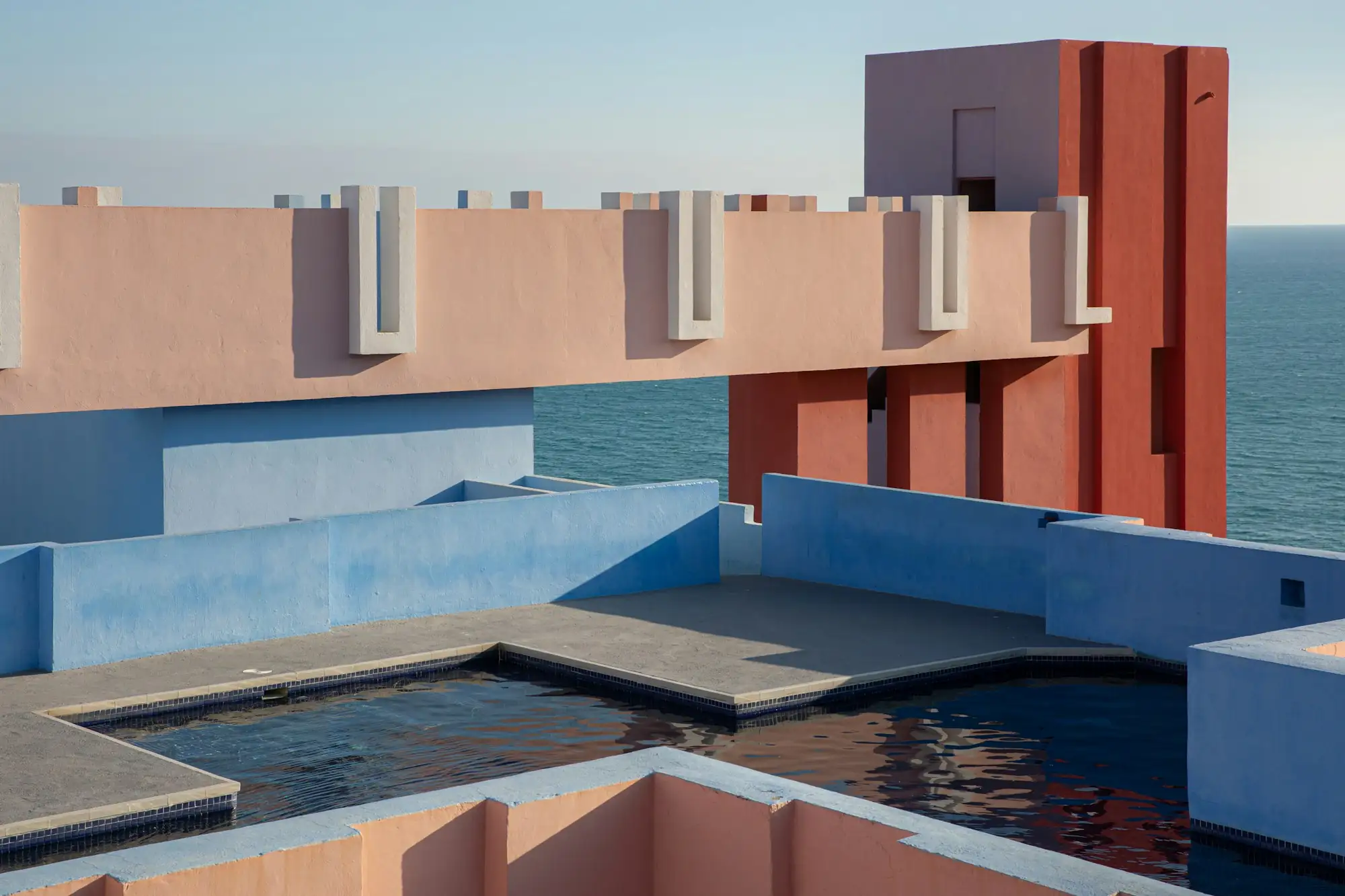 Pink and blue walls around a rooftop pool above the sea, at La Muralla Roja in Spain
